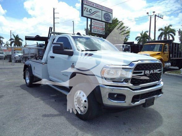 Tow truck with flatbed in a dealership lot showing RAM badge on grille and utility equipment in the bed.
