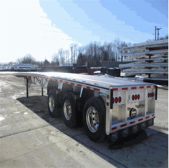 Tri-axle flatbed trailer with aluminum deck and rear multi-light configuration, three axles with dual tires, MAC logo on rear, reflective safety striping along sides.