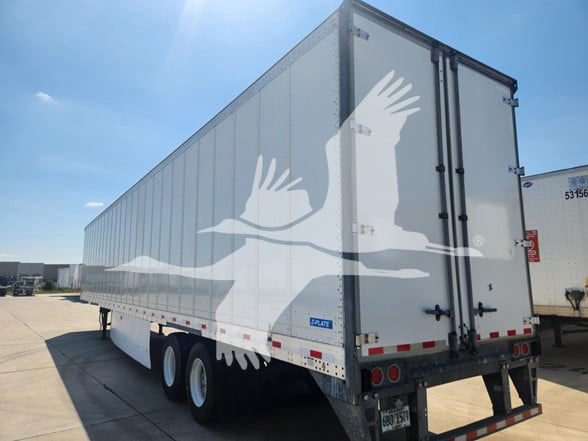 A 2019 Stoughton trailer with a rear double-door, three-axle configuration, silver exterior, and company logo silhouettes overlay. Visible text includes stock number plate and rear lights.