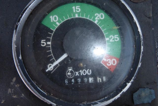 Backhoe dashboard gauge showing tachometer with green zone 0-25, red zone at 30, and hour meter digits x100.