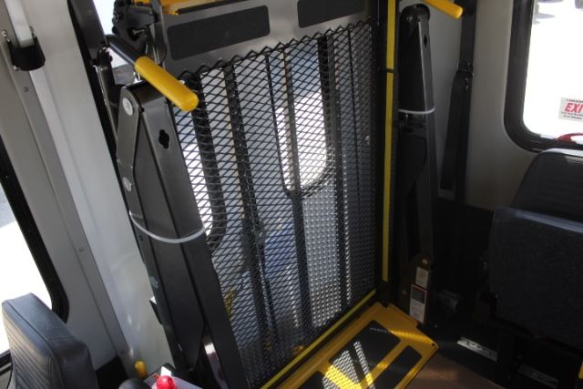 Ford E-450 shuttle bus interior showing a deployable mobility ramp or platform with yellow handles and a metal mesh gate.