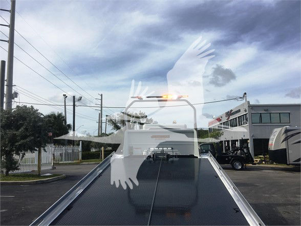 Flatbed tow truck with elevated cab; windshield text not legible from distance. Peterbilt emblem cannot be clearly read; background shows dealership building.
