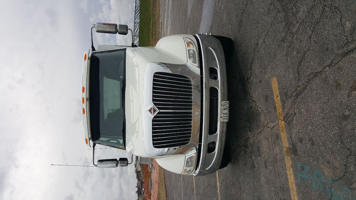 International truck front view in white with prominent chrome grille and bumper, side mirrors, and small orange cab lights on top.