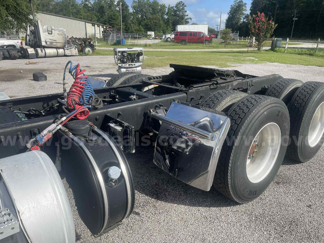 Peterbilt 386 cab and chassis rear showing triple rear axles and fuel tanks with chrome toolbox and coiled air hoses.