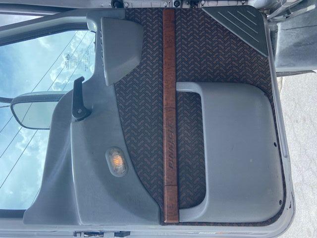 Truck door interior with patterned panel, lighted sensor, armrest, and a wooden grab handle labeled 'Pinnacle' across the middle.