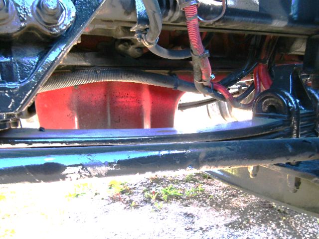 Kenworth T680 undercarriage showing red fuel tank and various wires and hoses amid black chassis members.