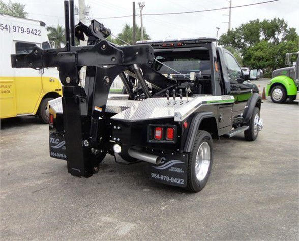 Tow truck rear/side view showing a hydraulic arm and toolbox with diamond plate surface. Visible text includes a phone number on the fender, and the back supports.