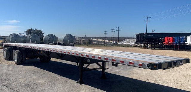 New 2024 48ft flatbed trailer with dual rear axles and extended platform, showing its aluminum deck and undercarriage in a yard.