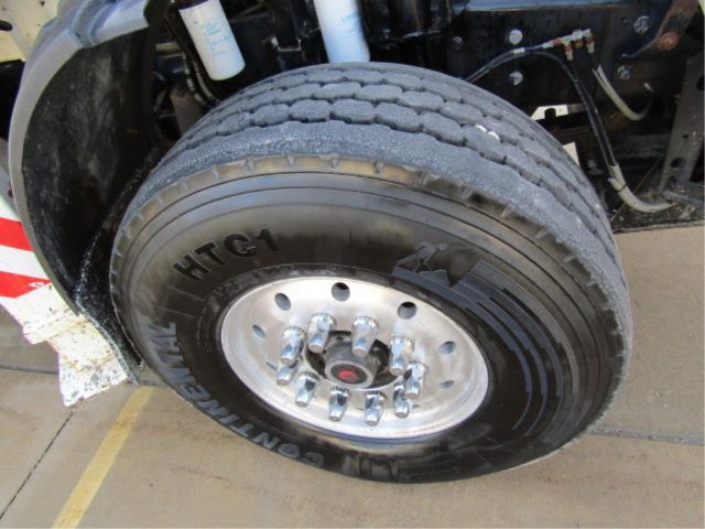 Truck front wheel with large tire, wheel hub, and visible suspension components under a Mack T310M truck.
