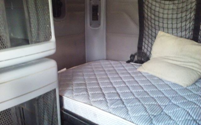 Interior sleeper cab of a 2006 Freightliner conventional truck showing a quilted mattress and pillow, with partition and storage netting.