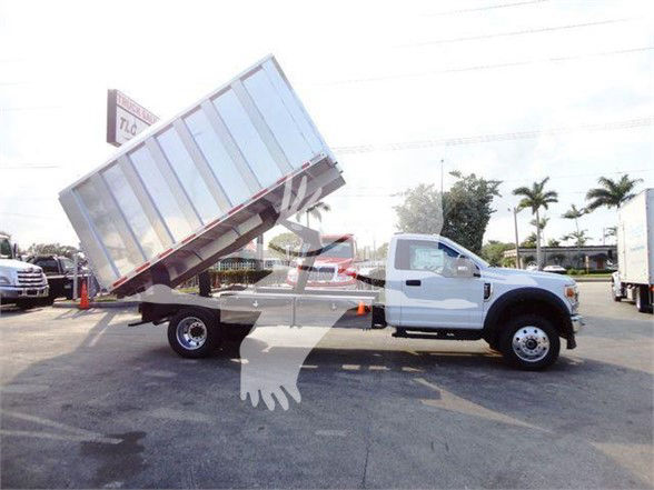 Ford F-600 dump truck in a dealership lot with a tilted dump bed. White cab, dual rear wheels, large cargo bed raised at a steep angle.