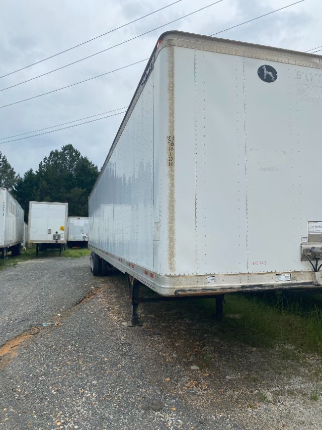 Trailer side view showing white Wabash Duraplate trailer with raised wheel wells and landing gear at front, gravel lot, other trailers in background.