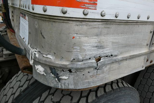 Great Dane trailer rear corner with damaged and cracked aluminum skin near wheel, visible rivets and orange stripe.