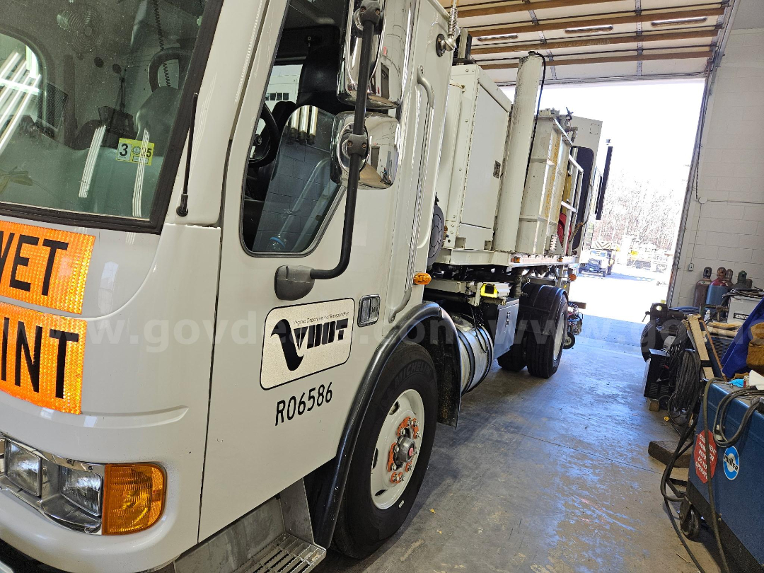 Truck cab side with Sterling logo and R06586 number, large orange 'YET' sign on door, long trailer with equipment, inside workshop.