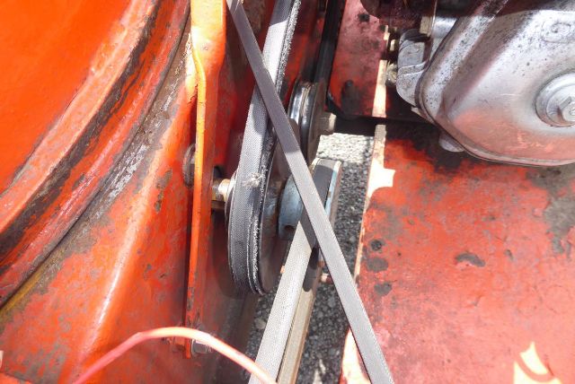 Equipment image showing a belt-driven pulley system and metal components on orange agricultural machinery. Visible text or labels are not legible.