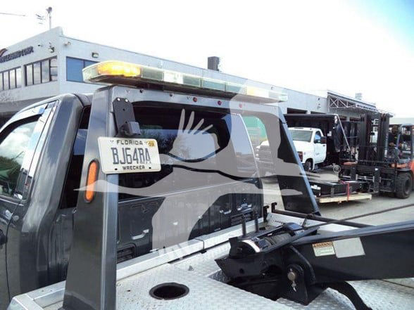Ford F-450 tow truck with light bar on top, Florida license plate visible in rear window, rear bed and hydraulic equipment in view.