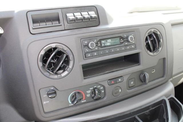 Dashboard of a 2024 Ford E450 with circular air vents, radio, climate controls, and storage compartment.