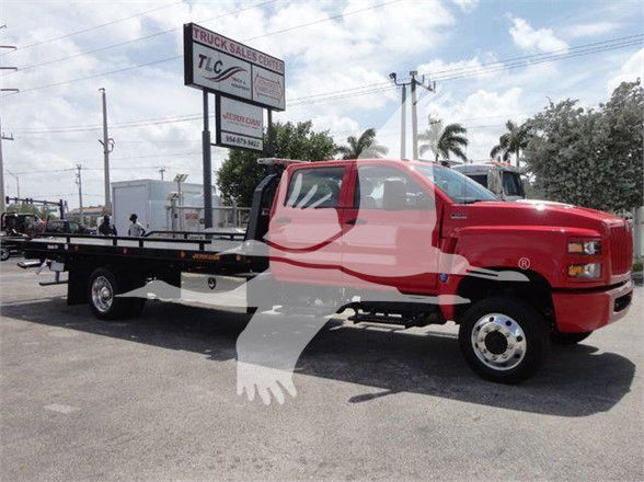 Tow truck with red cab and black flatbed, showing stock number J26674 in a dealership lot.