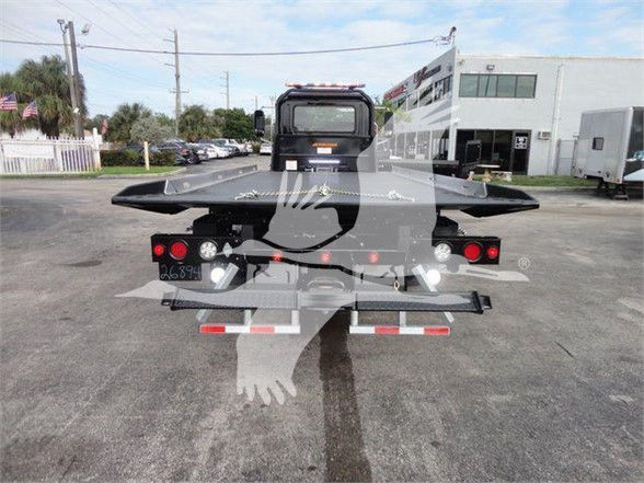 Rear view of a new 2023 Mack MD6 tow truck with a flatbed, taillights, and support equipment visible.