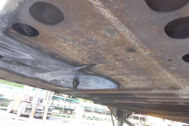 Underbody of a trailer showing rust-prone area and structural plate with circular cutouts; dirt and wear visible along the surface.