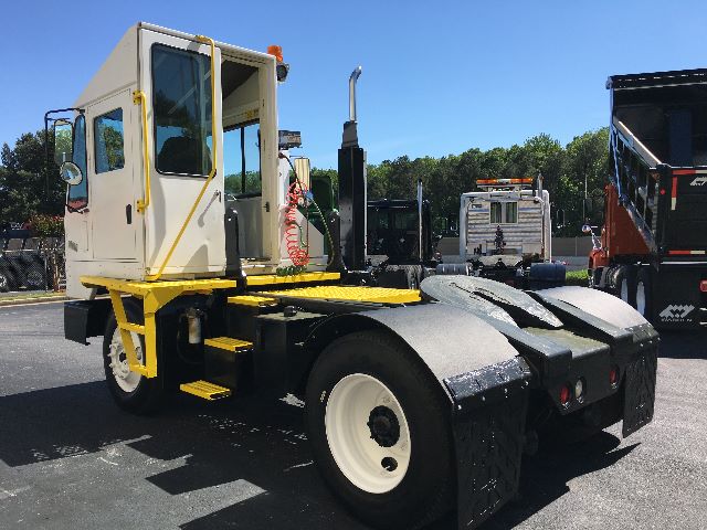 Industrial yard truck tractor unit with white cab, yellow steps, and black chassis. Side view shows sleeper cab, orange beacon light, and front engine area.