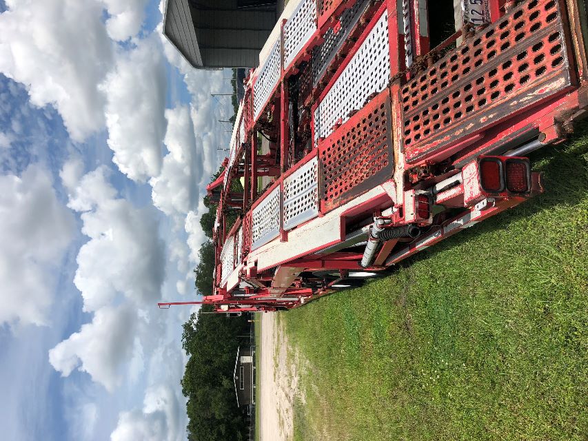 2007 Peterbilt 379 car carrier trailer with red and white perforated metal ramps parked on grass beside a building.