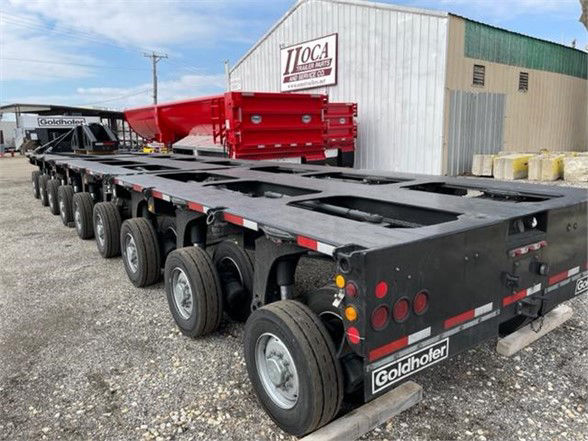 Trailer with multiple axles and a red hopper/deck attachment, Black Goldhofer trailer showing multiple wheels and rear lights.