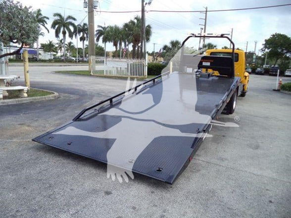 Flatbed tow truck with a long black metal ramp in an outdoor lot.