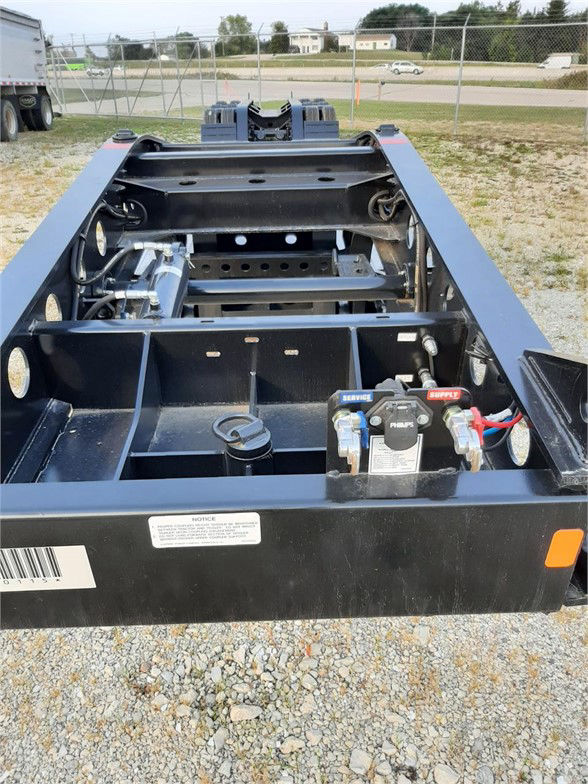 Lowboy trailer frame with hydraulic system and battery disconnect levers visible at the front right, spare components, and open deck support structure.
