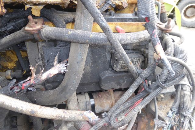 Engine bay with hoses, wiring, and a rusted exhaust pipe. Visible text includes no clear labels due to dirt.