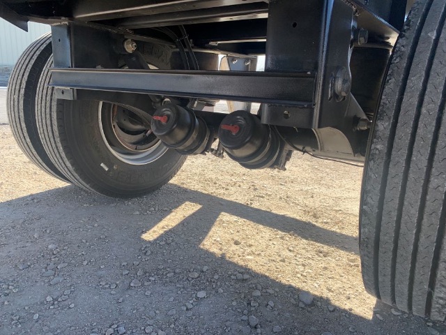 Flatbed trailer axle with dual air/electrical hoses and wheel tread visible.