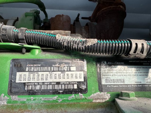 Under-hood view of a green John Deere engine bay with label plates and a black corrugated wiring loom.