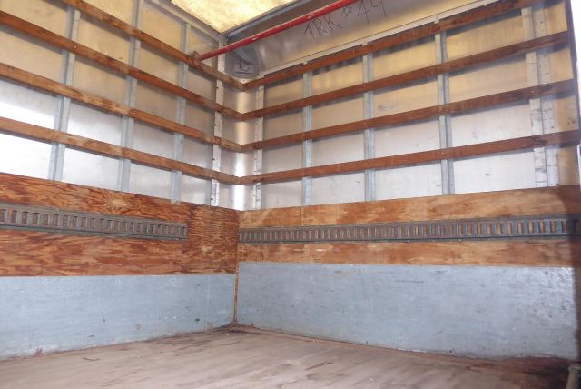 Interior of a truck box showing wooden side beams, steel rails, and plywood floor with metal trim along the lower walls.