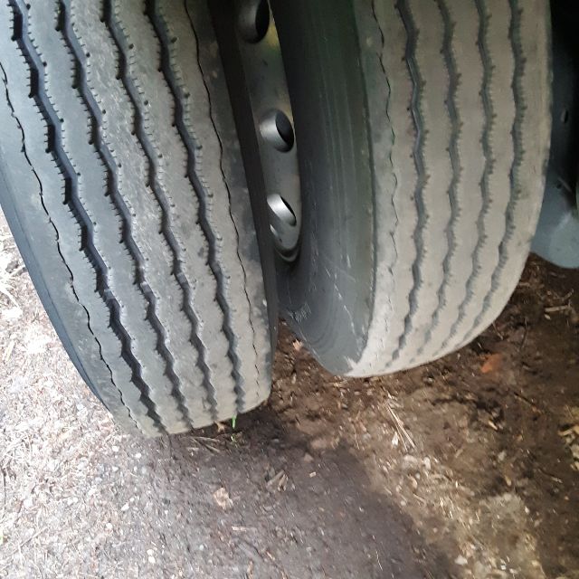 Two truck tires mounted on a Fontaine Revolution 52 trailer, dual rear axle with visible treads and metal hub, dirt ground.