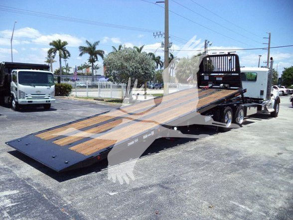 Kenworth T880 flatbed tow truck in a dealership lot with a long wooden deck and a white cab in the background.