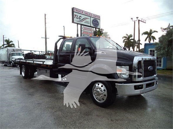 Ford F750 tow truck in view showing front and flatbed with branding visible on cab and chrome bumper.