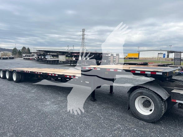 Trailer side view showing a drop deck expandable middle lift trailer with multiple axles and a white wheel on the near rear.