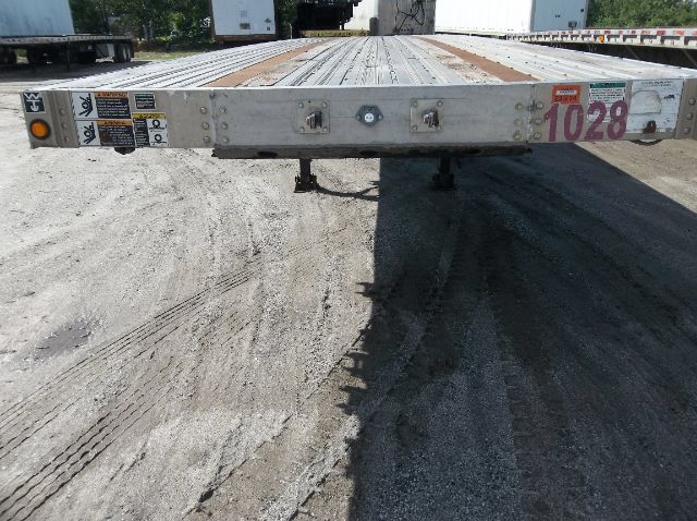 Front view of a used 2009 Wilson flatbed trailer showing rear end with access latches, safety stickers, and a handwritten purple number 1028.