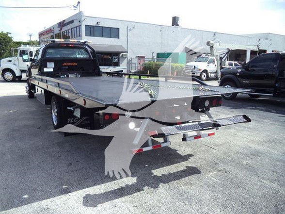 Tow truck flatbed trailer hitch on International CV truck, dual rear lights, reflective tape, and rugged flatbed with wheel chocks in a lot.