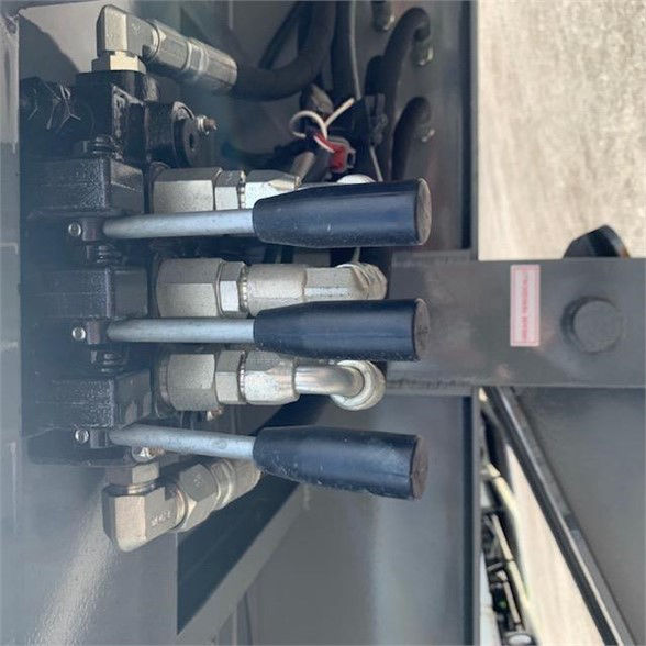 Trailer hydraulic control valves with hoses and fittings in a container delivery trailer; multiple blue lever handles and metal fittings.