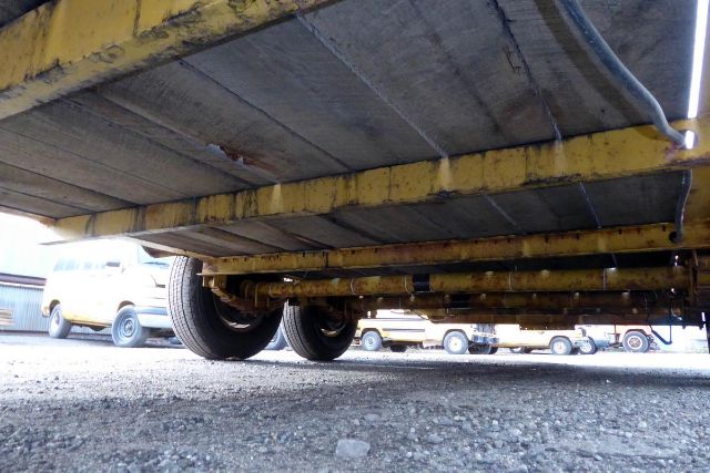 Trailer undercarriage showing yellow painted rails and wheels, ground-level view of payload frame.