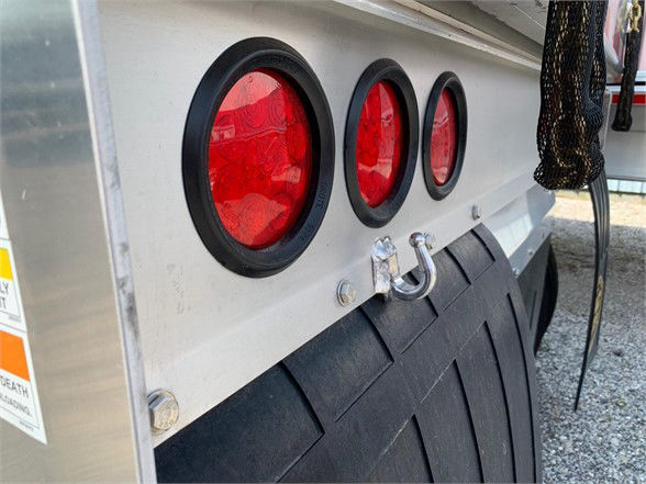 Trailer rear showing three red circular taillights, a silver aluminum surface, a U-bolt latch, and a black mudflap.