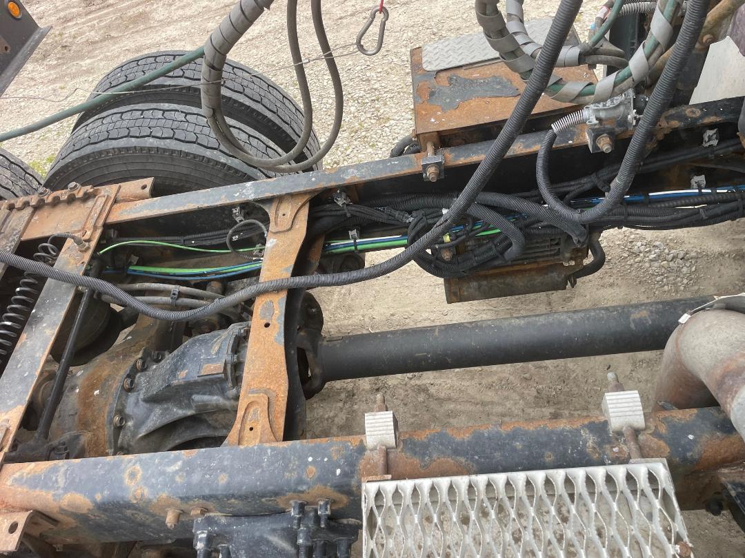 Chassis frame of a Freightliner Cascadia 125 truck showing exposed wiring harnesses, rusted frame, rear drive shaft, and parts of the truck’s undercarriage.