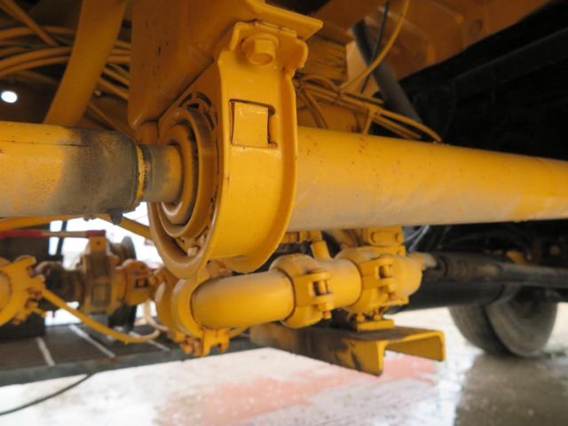 Truck undercarriage showing yellow suspension leaf and drive shaft with U-bolts and mounting brackets.
