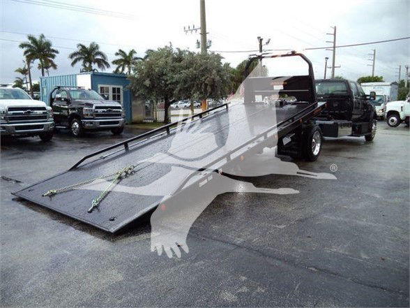 Tow truck with a folded flatbed on a dealership lot; no legible labels visible on the flatbed area.