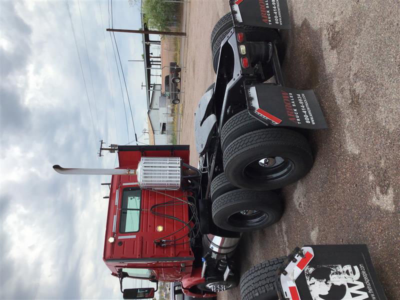 Truck chassis and dual rear axles with red Volvo cab, fuel tank, and tags hanging from rear wheels.