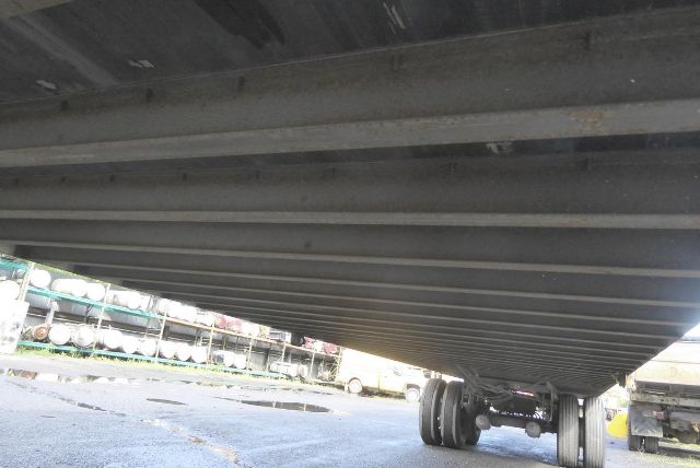Trailer underside showing frame rails and tires, with storage yard in background.