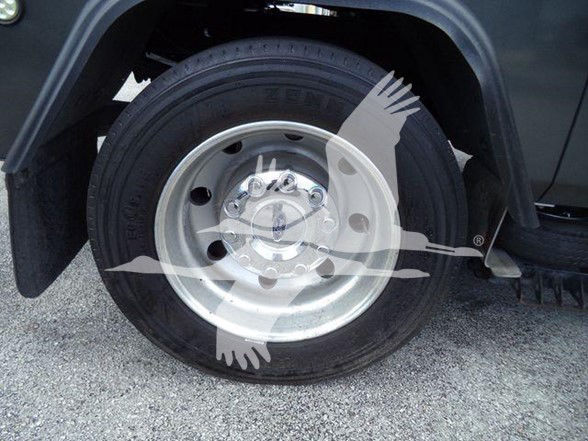 Wheel and tire on a Ford truck with a circular watermark overlay; wheel hub shows lug nuts.