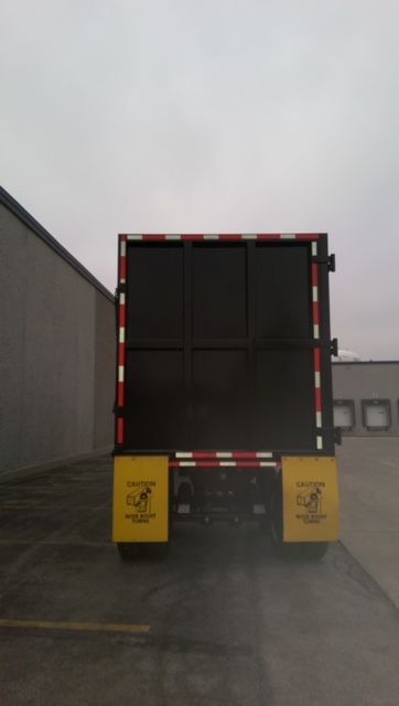 Back of a Great Dane 40 ft dump trailer with black tailgate and yellow safety chutes. CAUTION labels on lower rear with text.