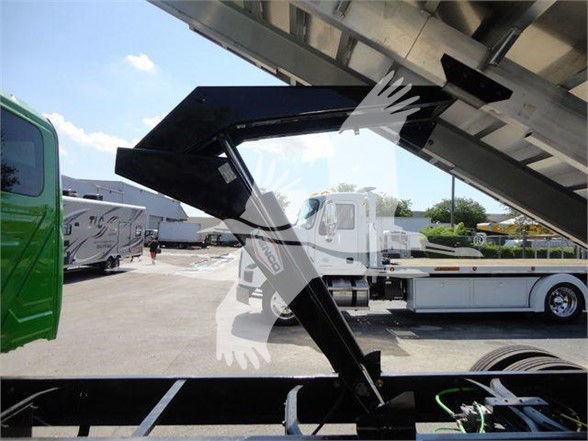 Truck bed or chute of a 2023 International MV with hydraulic arms and metal framework, chassis visible in foreground and other trucks in background.